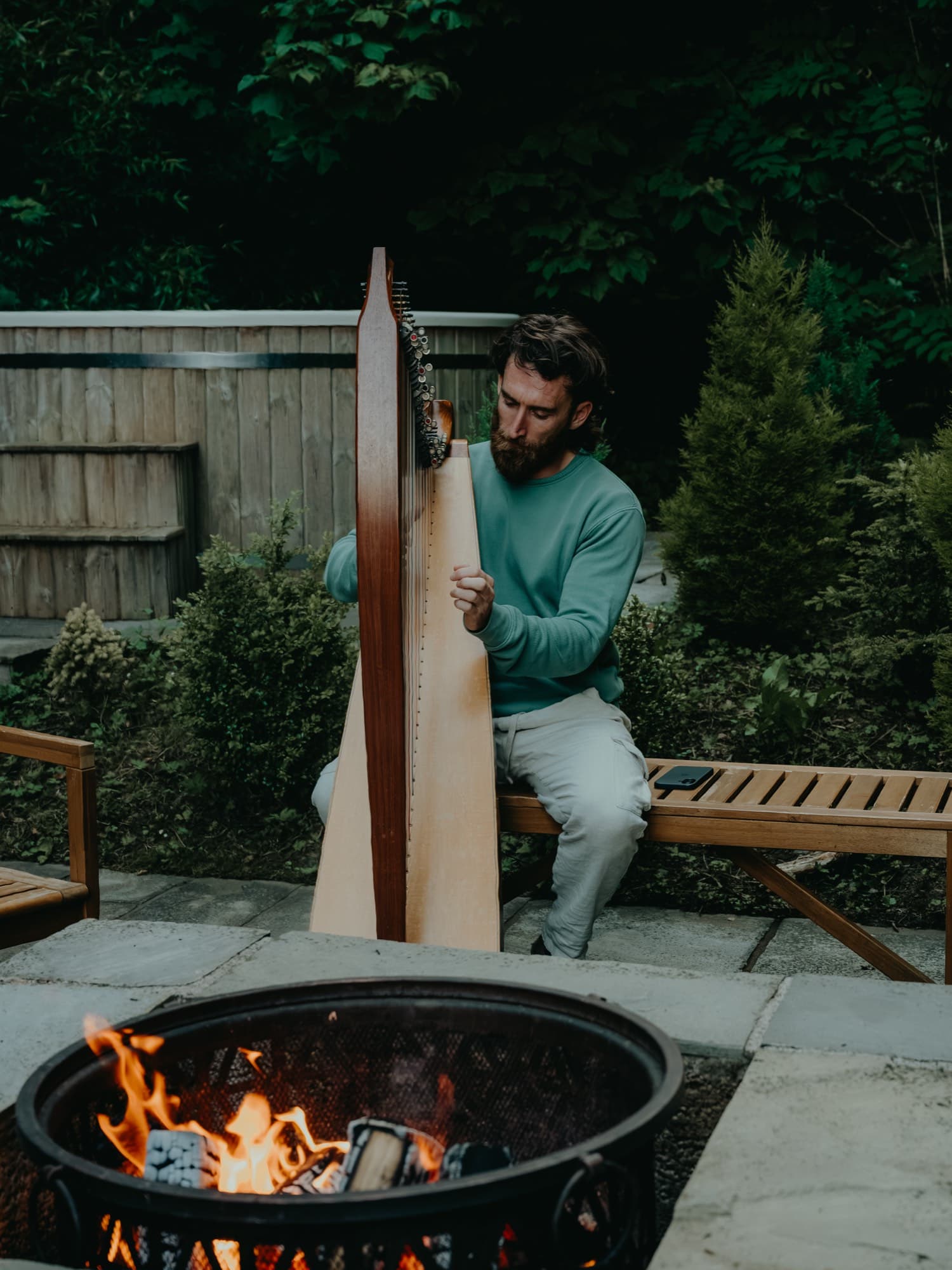 A participant playing a harp beside the fire pit at dusk